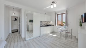 A modern kitchen with a dining area, white cabinetry, and a large window. - Apartamenty Sun & Snow Zasypane Mazury (gmina Malkinia Gorna)