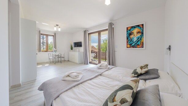 A modern bedroom with a large bed, a desk, and a view of the outdoors. - Apartamenty Sun & Snow Zasypane Mazury (gmina Malkinia Gorna)