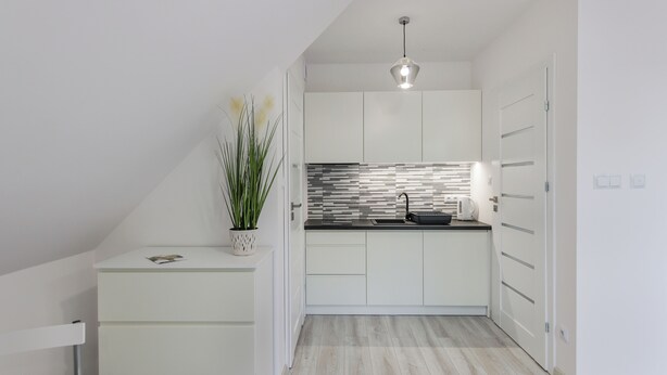 A modern kitchen with white cabinetry, a black countertop, and a backsplash with a striped pattern. There is a potted plant on the counter and a hanging light fixture above. - Apartamenty Sun & Snow Zasypane Mazury (gmina Malkinia Gorna)