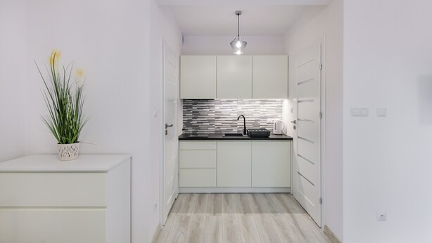 A modern kitchen with white cabinets, a black countertop, and a striped backsplash. - Apartamenty Sun & Snow Zasypane Mazury (gmina Malkinia Gorna)