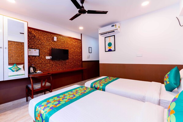 A hotel room with two beds, a desk, a TV, and a ceiling fan. - Treebo Emirates Suites Indiranagar (Bangalore)