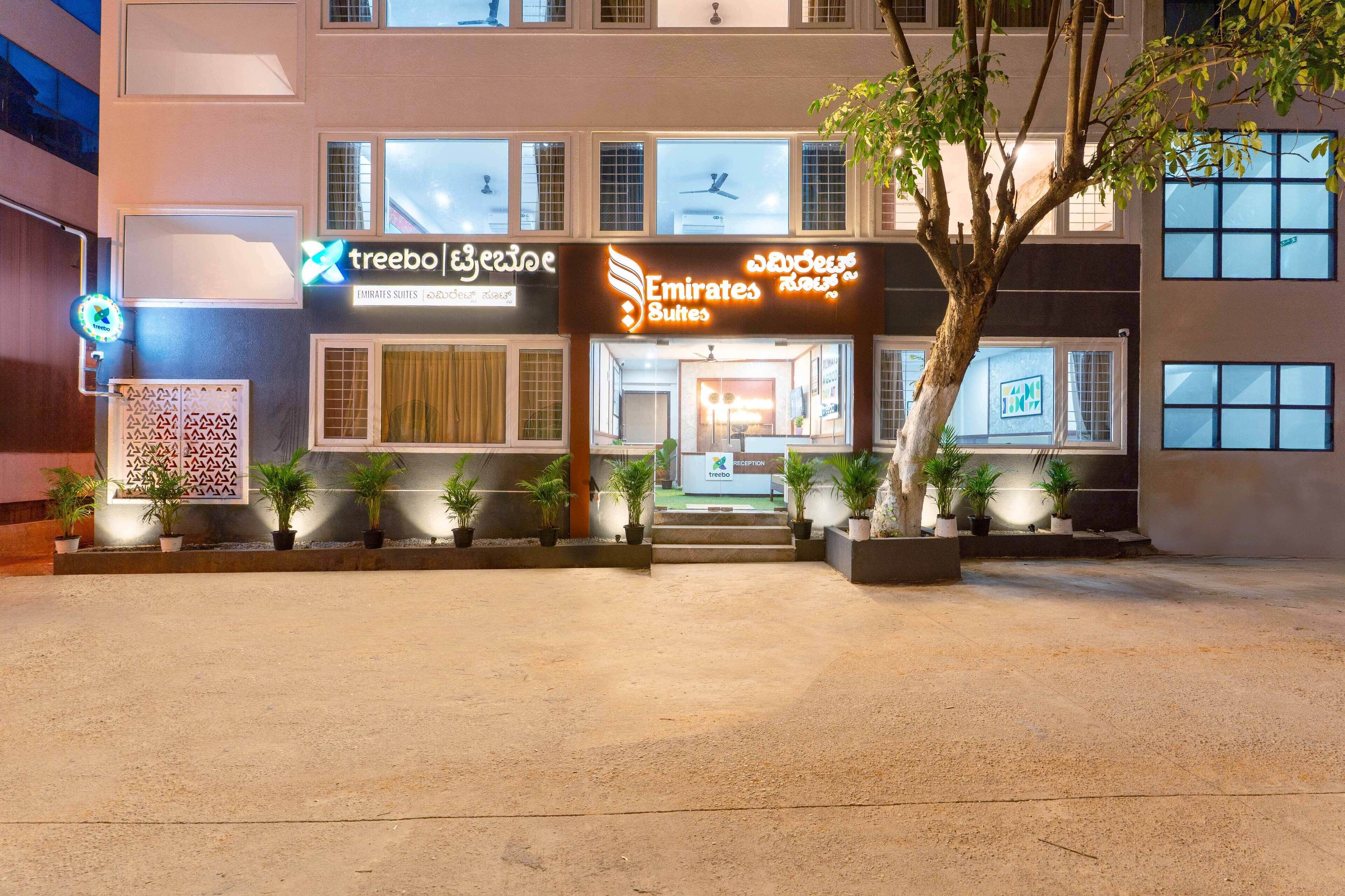 A hotel with a sign for Emirates Suites, multiple windows, and potted plants in front.