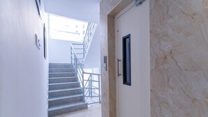 A hallway with a marble wall, a door with a black handle, and a staircase with metal railings. - Treebo Emirates Suites Indiranagar (Bangalore)
