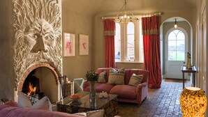 Un salon chaleureux avec une cheminée, un canapé rose et un lustre.