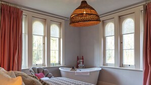 Une chambre avec un grand lit, une fenêtre avec des rideaux, une baignoire blanche et un luminaire suspendu.