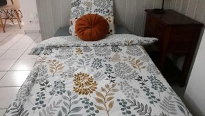 A bedroom with a floral-patterned bedspread, a single orange pillow, and three wall hangings above the bed. - SCALE BOURBON SEASONAL RENTAL (St Denis)