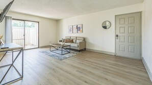 Een ruime woonkamer met een bank, salontafel en een eettafel. Er is een schuifpui naar een balkon.