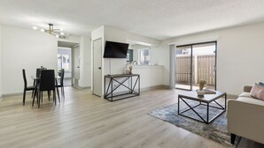 Een moderne woonkamer met een eethoek, een flatscreen televisie aan de muur en een schuifpui naar een balkon.