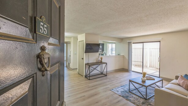 Een modern appartement met een houten vloer, een keukenhoek, een woonkamer met een bank en een grote schuifpui naar buiten.