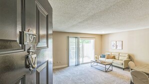 Een woonkamer met een beige bank, een bijzettafeltje en een deur met het nummer 197.