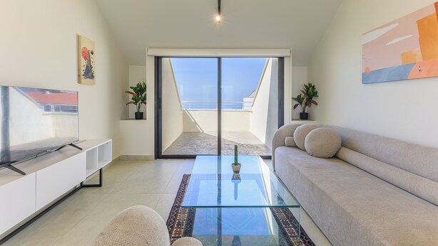 Ein modernes Wohnzimmer mit Glastisch, einer Couch, einem Flachbildfernseher und einem Balkon mit Blick.