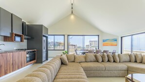 Ein modernes Wohnzimmer mit einer großen Eckcouch, einer Küche mit dunklen Schränken und großen Fenstern, die einen Blick auf die Stadt ermöglichen.