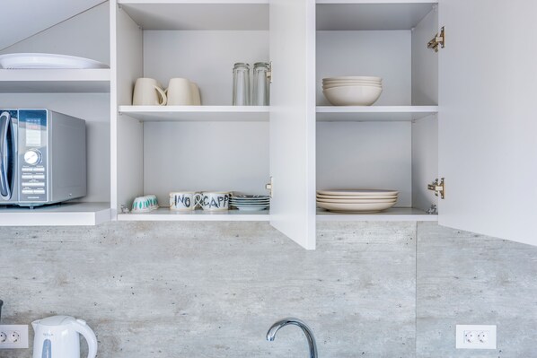 Una cocina con armarios blancos, hervidor, microondas y cafetera.