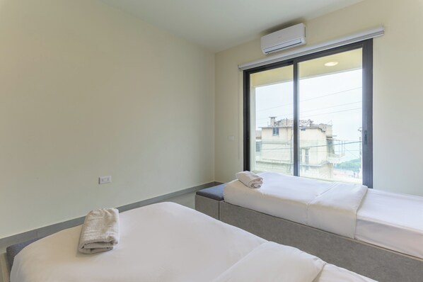 A hotel room with two beds, a large window, and an air conditioning unit. - Brummana Heights Apartments (Broumana)