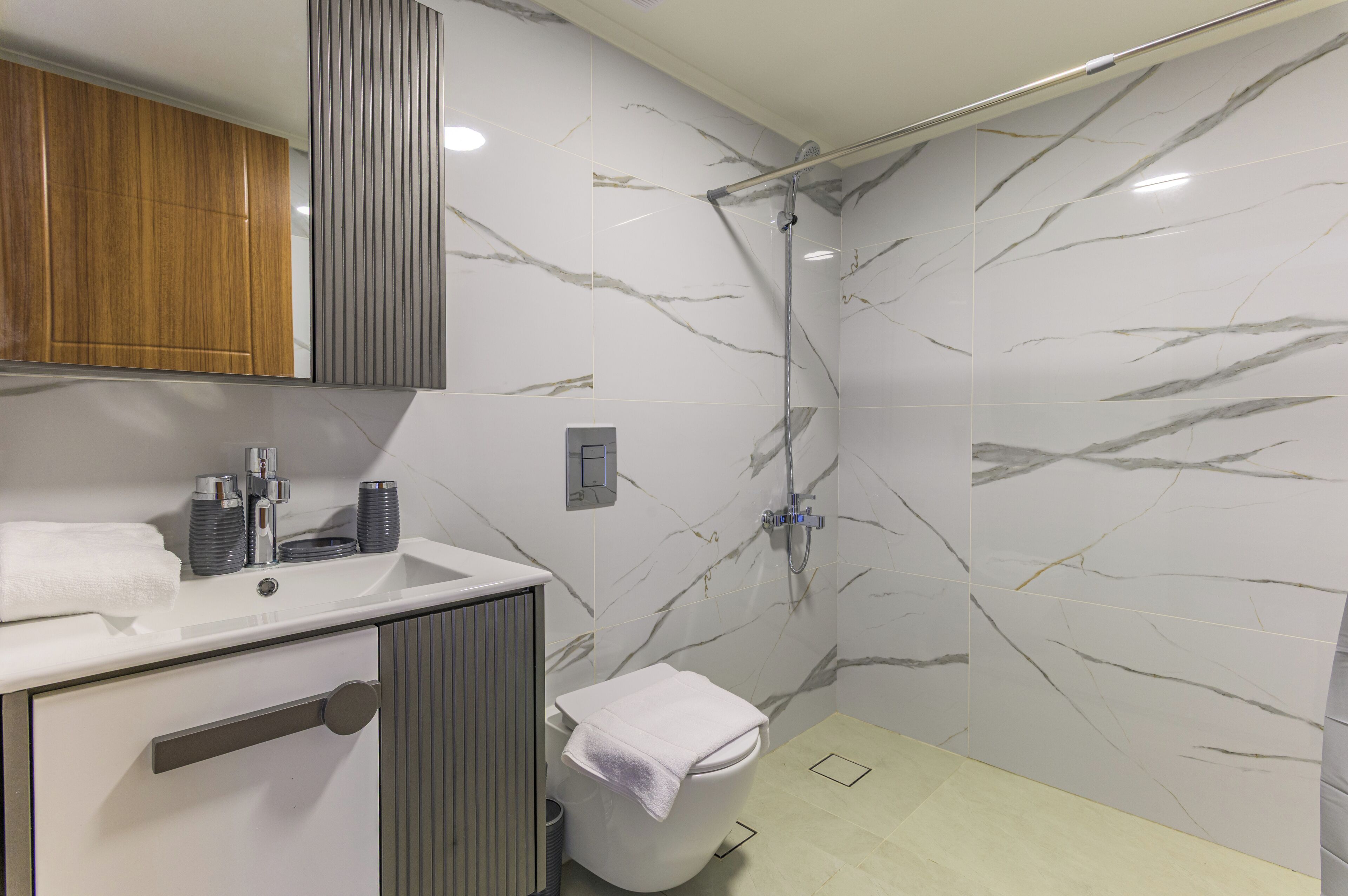 A modern bathroom with a marble shower wall, a sink with a mirror, and a toilet.