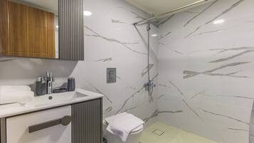 A modern bathroom with a marble shower wall, a sink with a mirror, and a toilet.