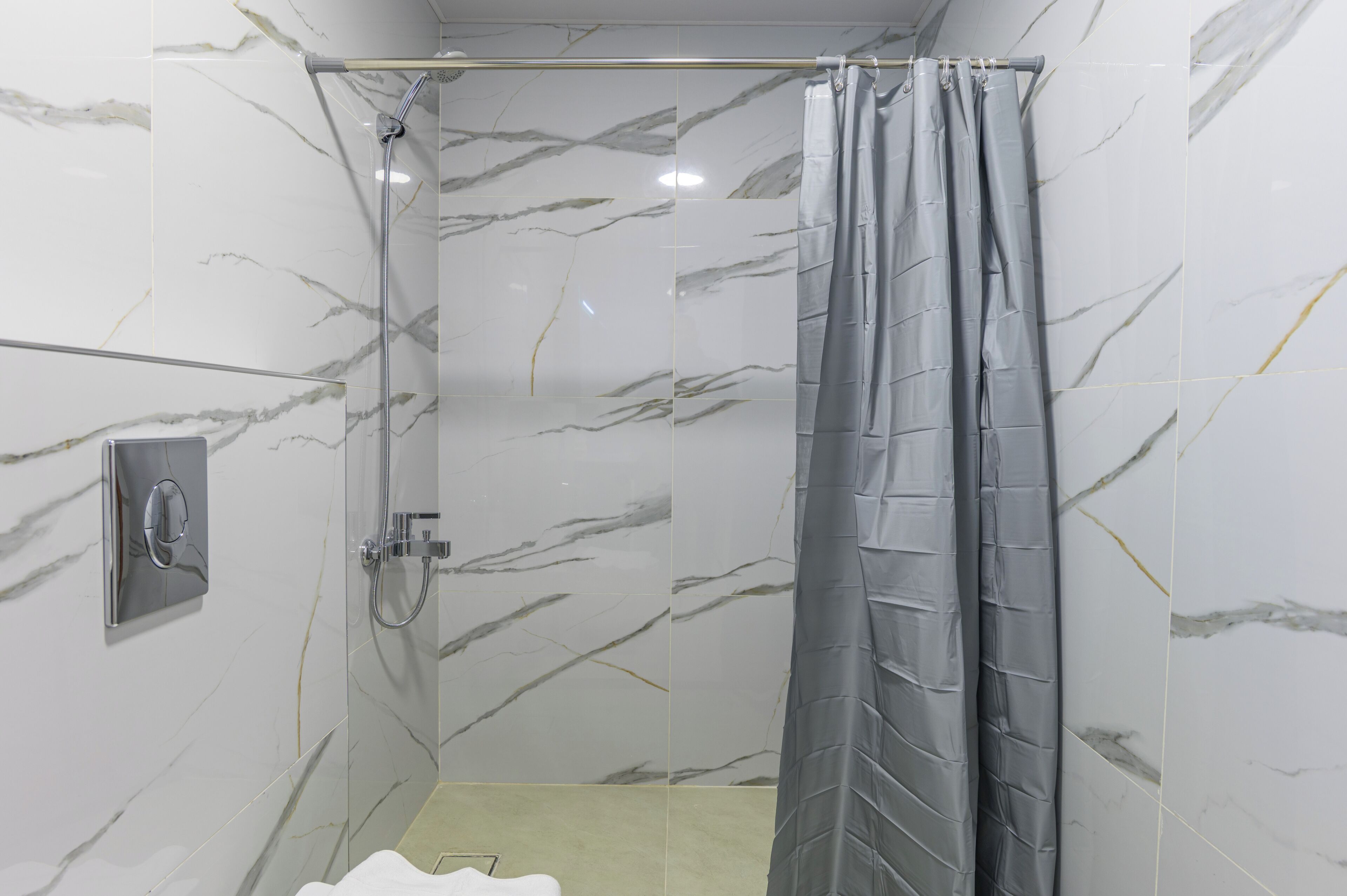 A shower with a grey curtain, a handheld showerhead, and a wall-mounted control panel.