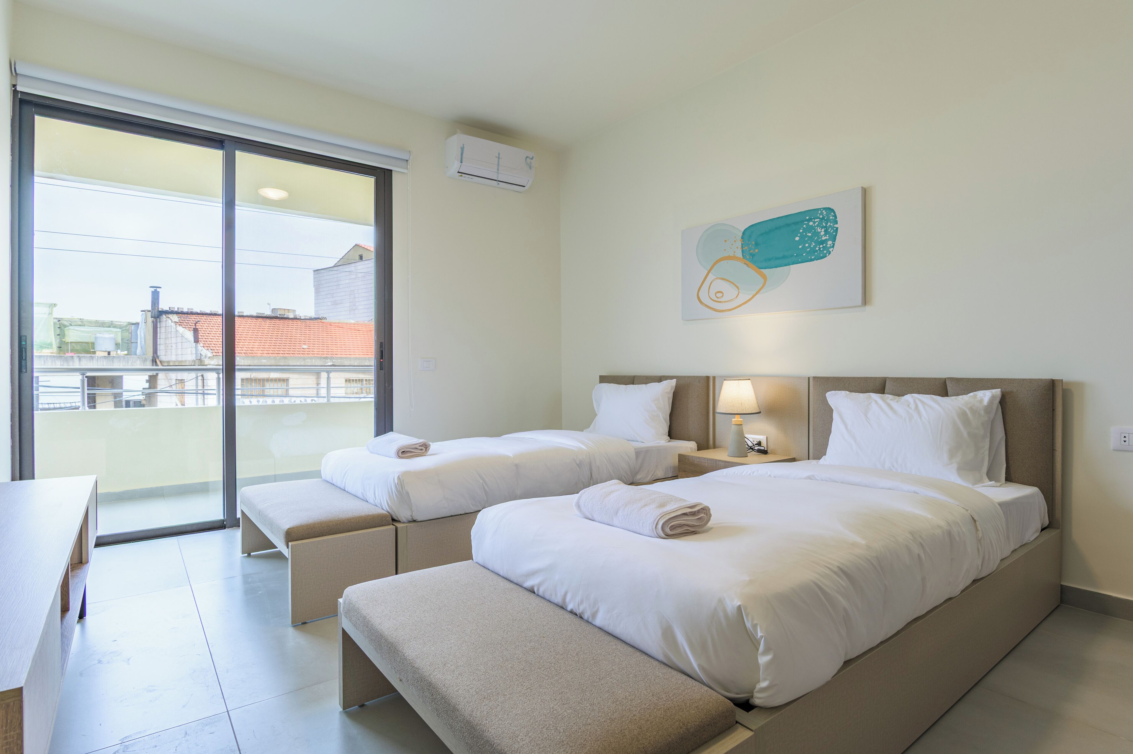 Habitación de hotel con dos camas, un banco, un escritorio y vistas al exterior.