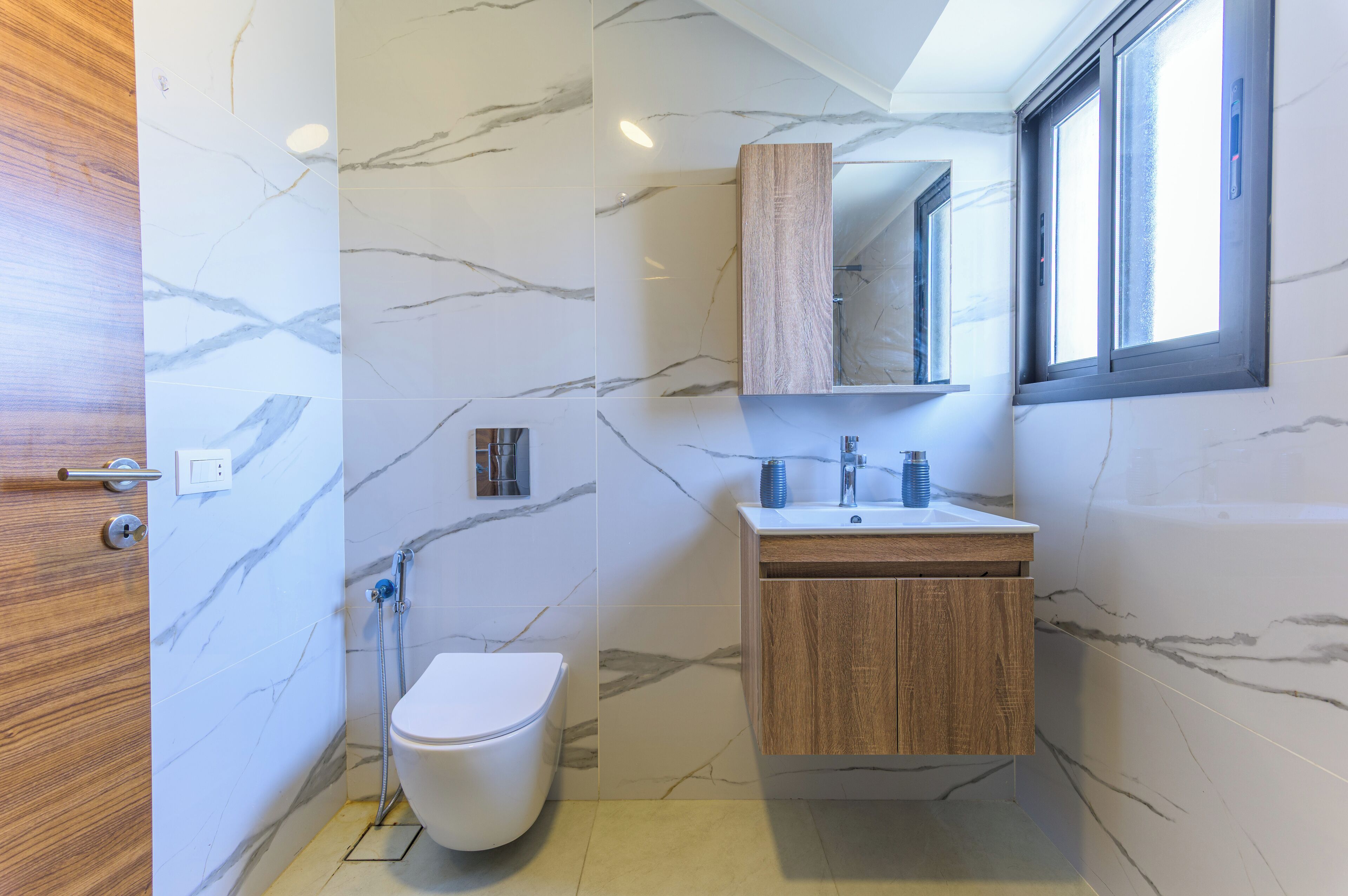 A modern bathroom with a marble wall, wooden vanity, and a toilet.