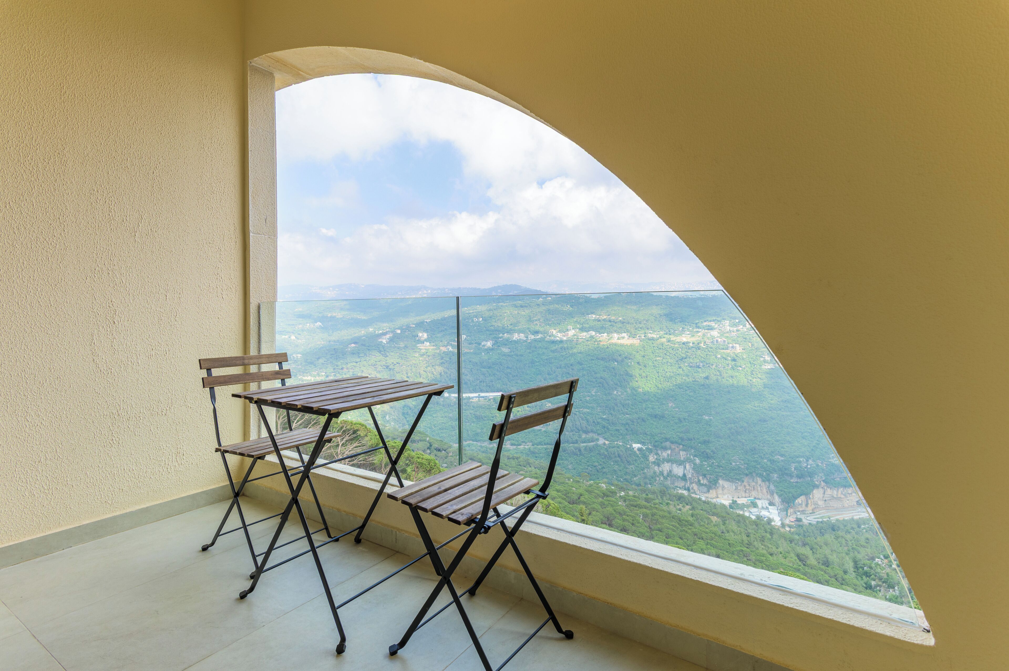 A balcony with two wooden chairs and a table, overlooking a mountainous landscape.