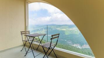A balcony with two wooden chairs and a table, overlooking a mountainous landscape.