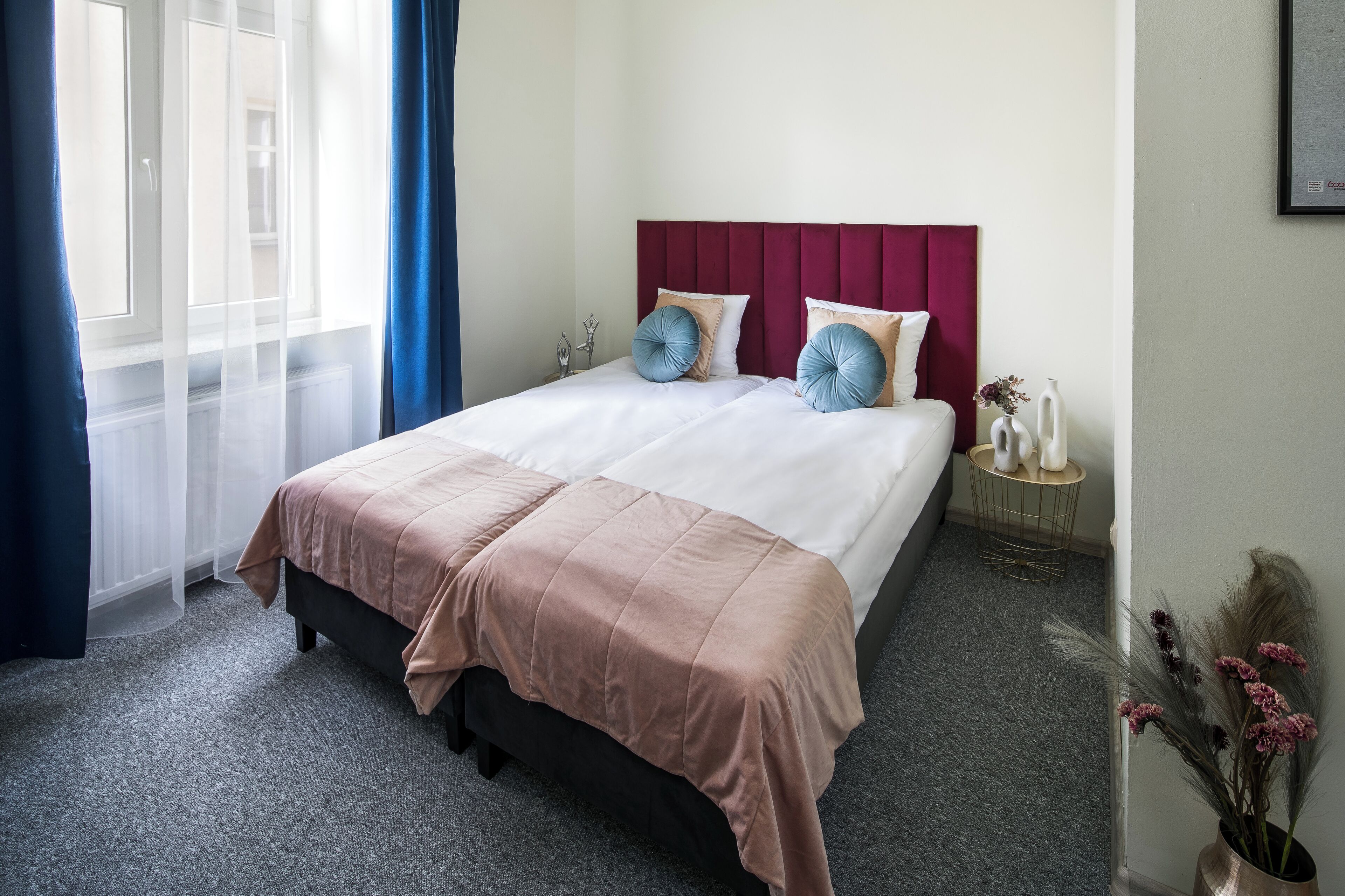 A neatly made bed with a pink and white bedspread, two pillows, and a red headboard.