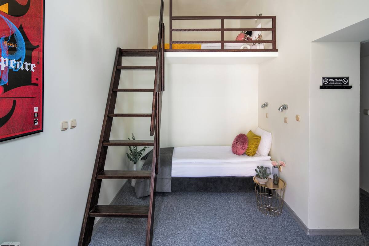 A bunk bed with a ladder, a small bedside table with a plant, and a sign on the wall.