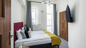 A hotel room with a bed, a bedside table, a TV mounted on the wall, and a wooden door. - The Royal Patch Aparthotel (Kraków)