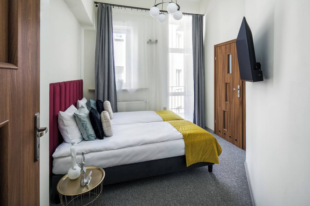 A hotel room with a bed, a bedside table, a TV mounted on the wall, and a wooden door.