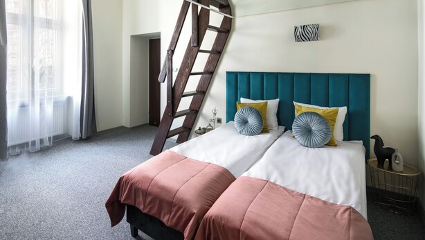 A bedroom with a bed, a wooden ladder, a teal headboard, and a small side table with decorative items. - The Royal Patch Aparthotel (Kraków)