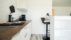A modern kitchen with white cabinets, a coffee machine, a kettle, and a bar stool. - Charming apartment in a fantastic location - 2 min. to the lake (Lohmen)