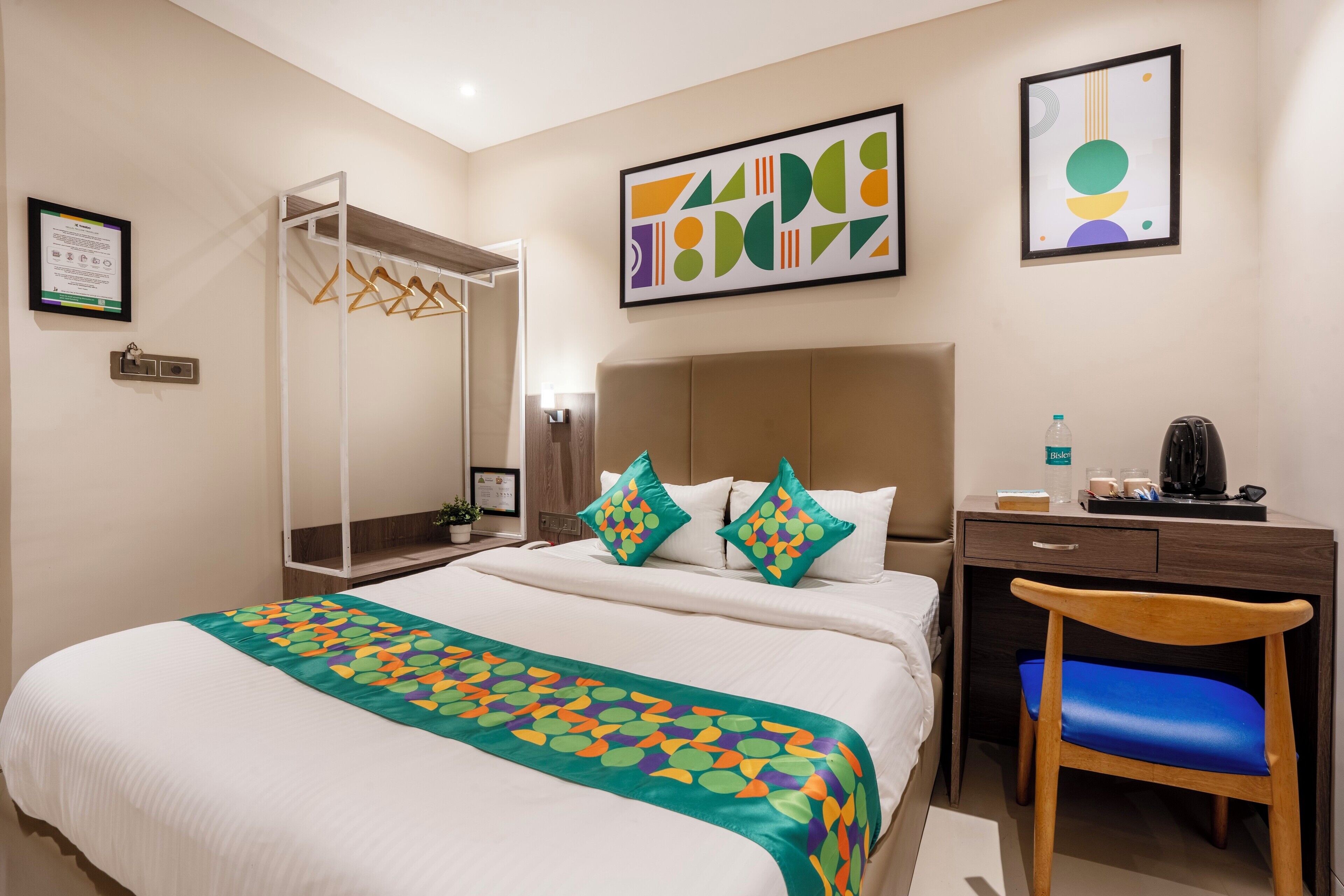 A hotel room with a bed, a desk, a chair, and artwork on the walls.