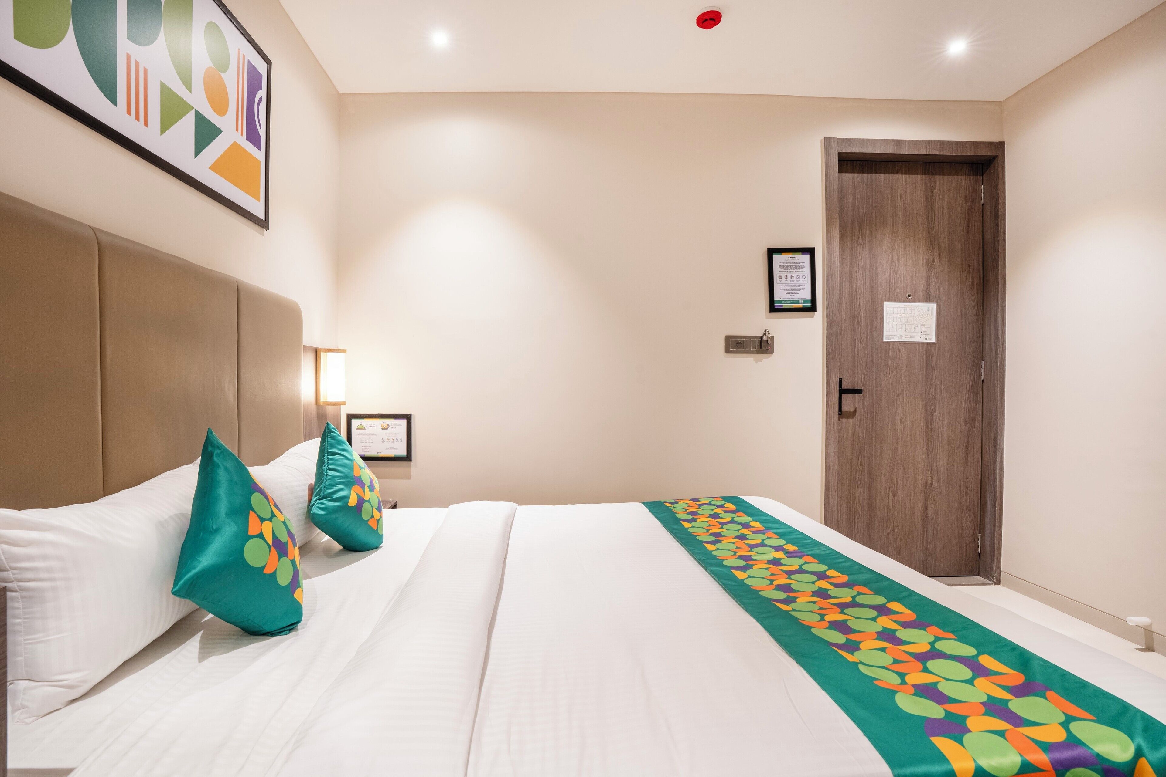 A hotel room with a large bed, a wooden door, and a framed picture on the wall.