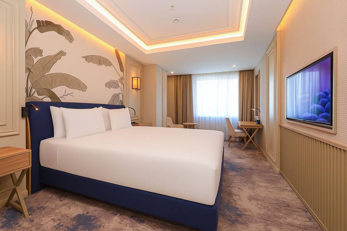 A hotel room with a large bed, a desk with a chair, a TV, and a window with curtains.
