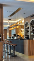 Zona de bar moderna con mostrador de madera, lámparas colgantes y taburetes.