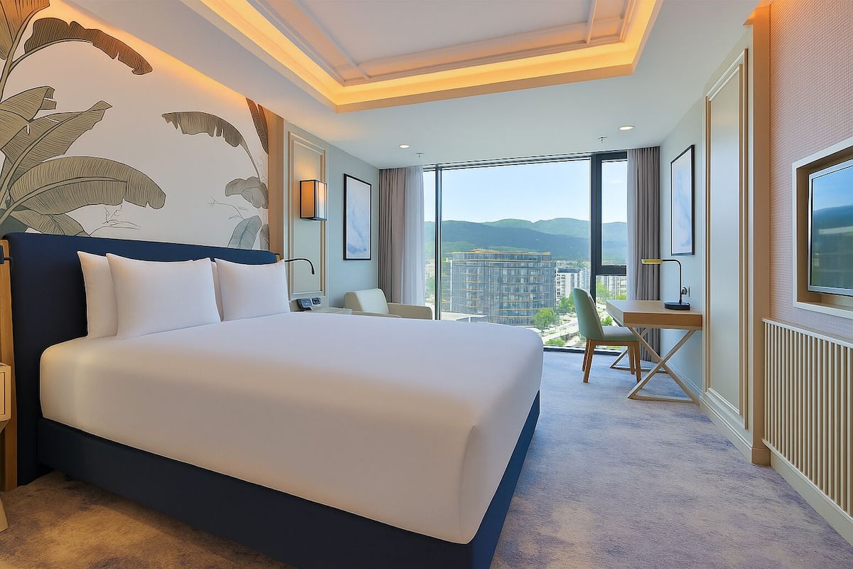 A hotel room with a large bed, a desk, and a view of a cityscape.