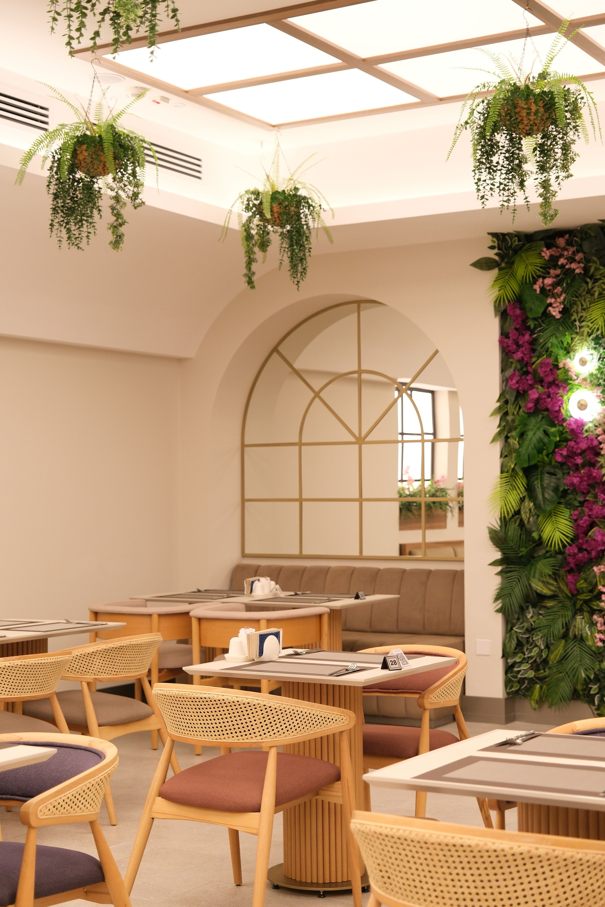 Un interior moderno con mobiliario de madera, plantas colgantes y un amplio ventanal de arco.