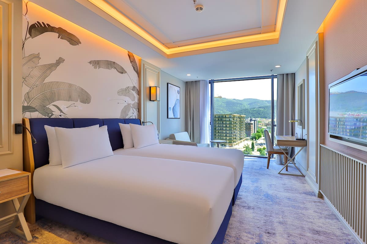 A hotel room with a large bed, a desk, and a view of the city.