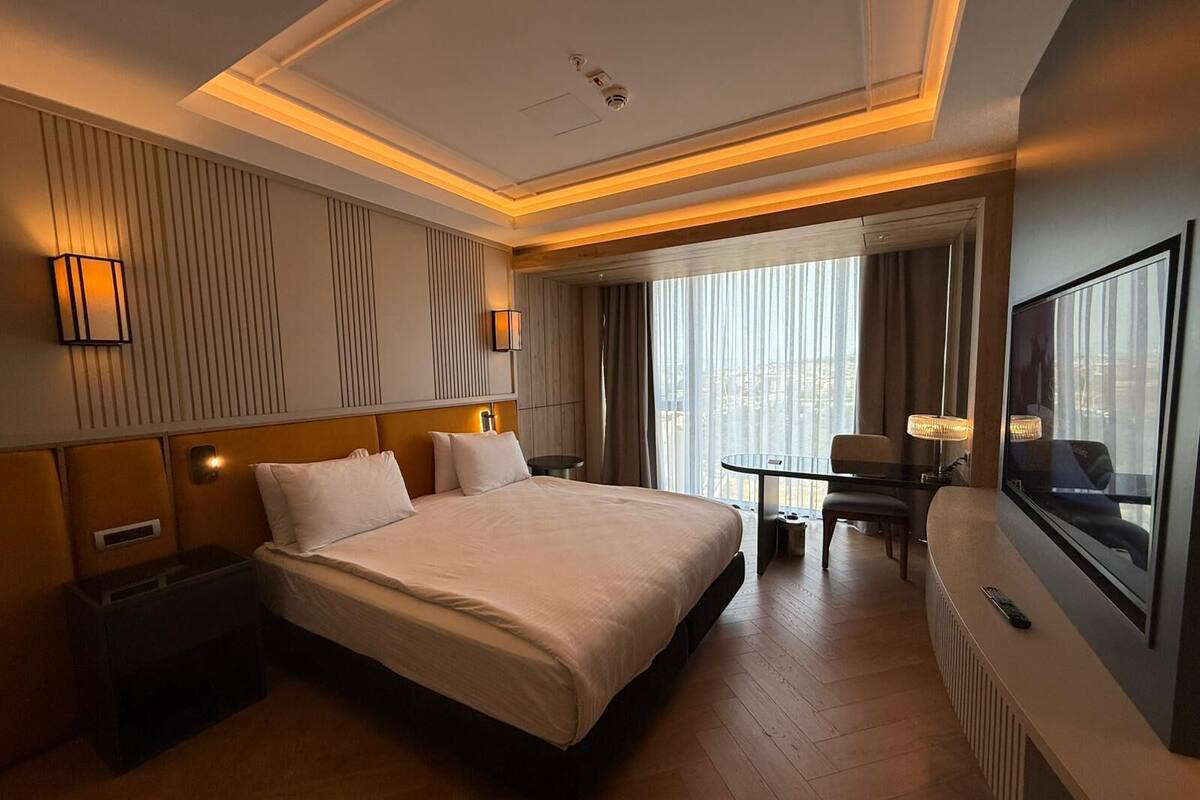 A hotel room with a large bed, a desk, a chair, a TV, and a window with curtains.