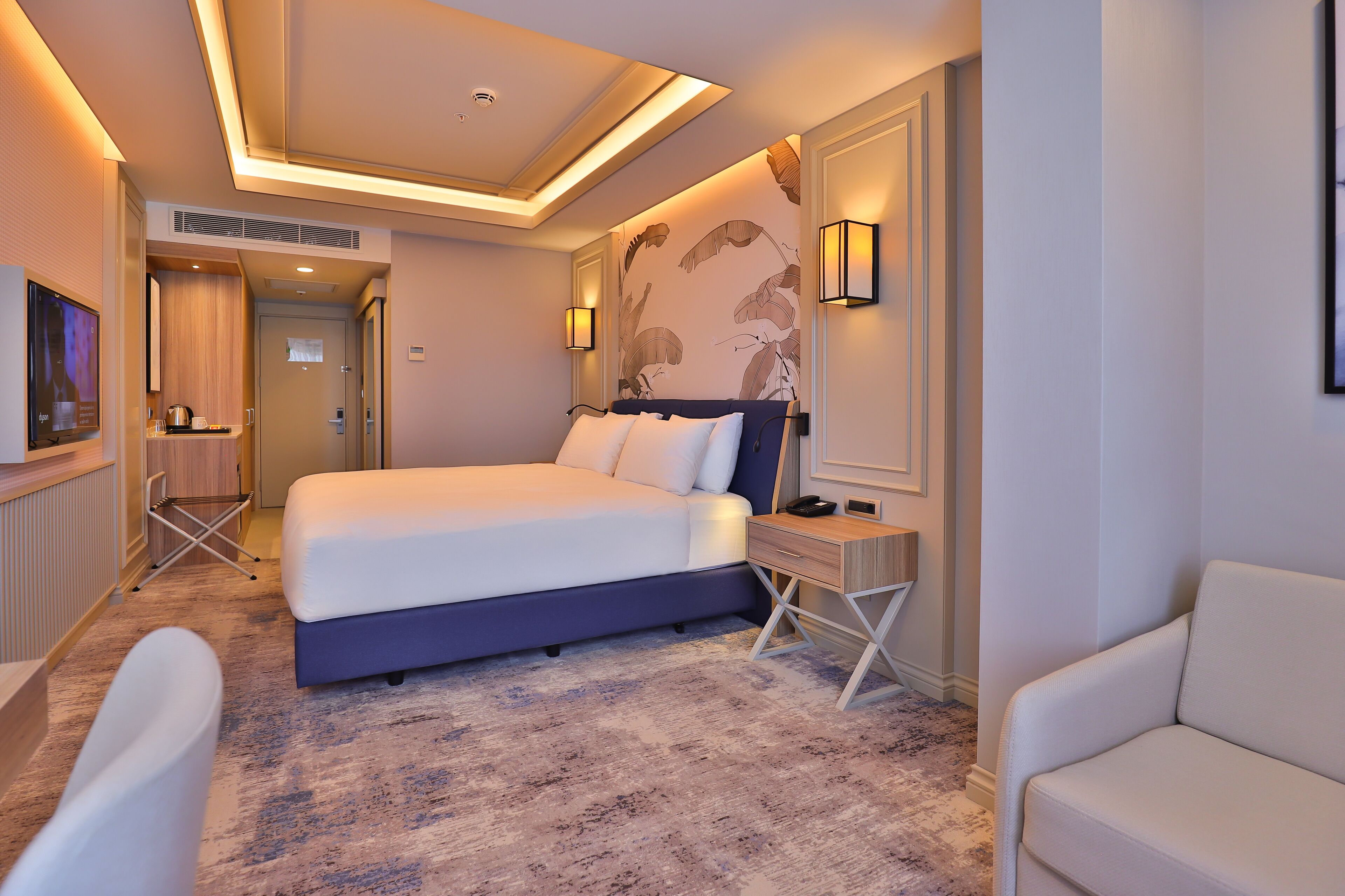 A modern hotel room with a large bed, bedside tables, a desk, and a TV.