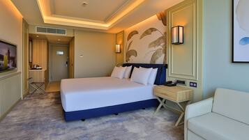 Una habitación de hotel con una cama grande, una mesita de noche con lámpara, una silla y un televisor.