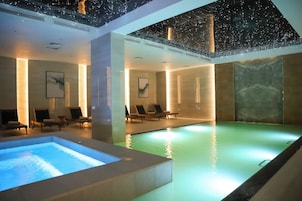 Una piscina interior moderna con un elemento acuático transparente, sillas de descanso y un techo con diseño de estrellas.