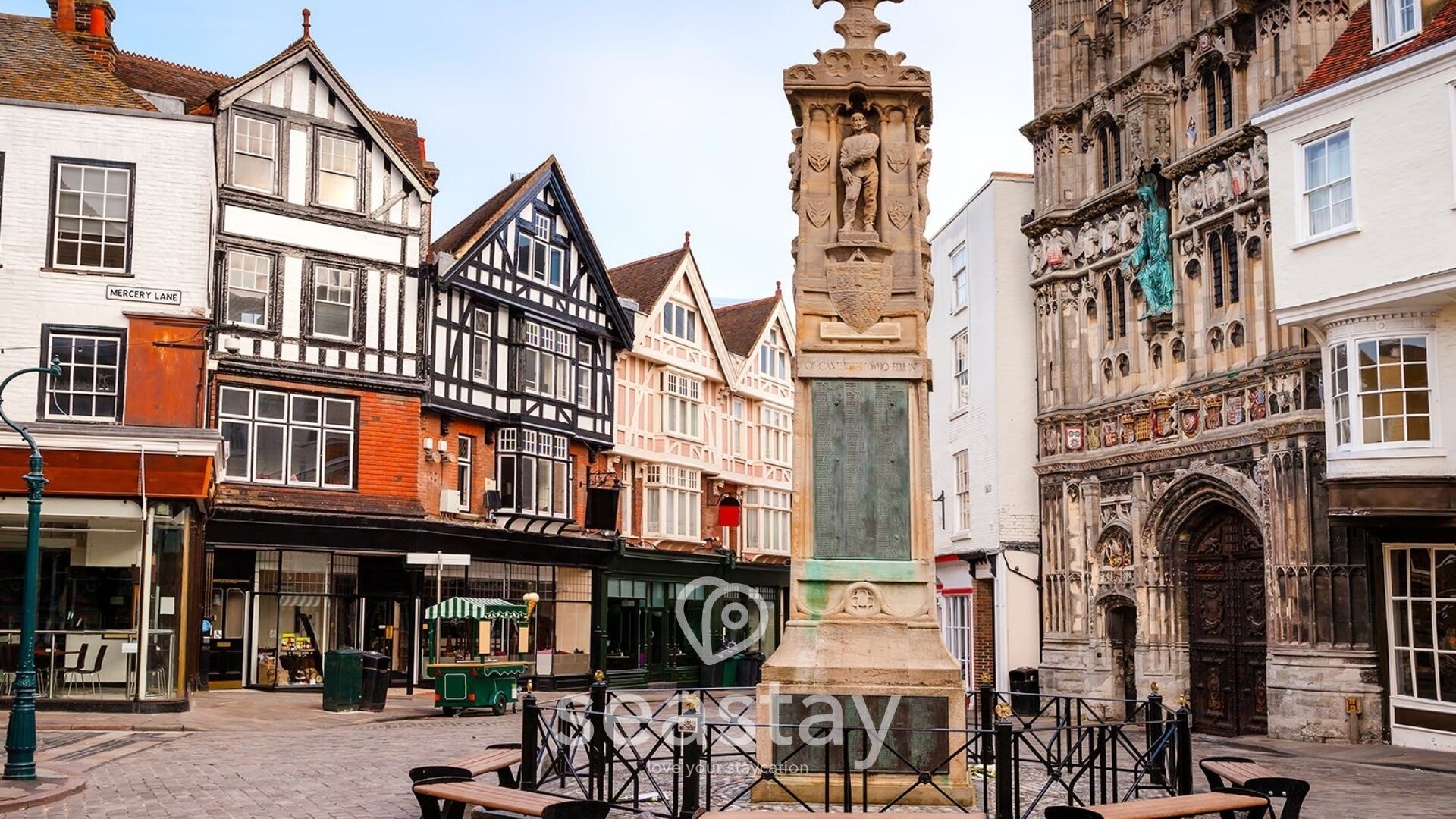 Une place historique bordée de bâtiments traditionnels à colombages, avec un monument central et une rue pavée.