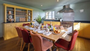 A kitchen with yellow cabinets, a wooden dining table set for four, and a stainless steel range hood. - Wilderness Reserve - Newt Cottage (Halesworth)