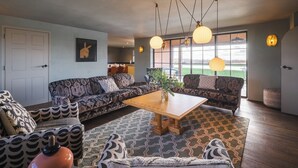 A living room with patterned sofas, a wooden coffee table, and pendant lighting. - Wilderness Reserve - Newt Cottage (Halesworth)