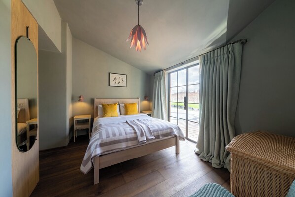 A bedroom with a bed, bedside tables, a mirror, a hanging light fixture, and a window with curtains.