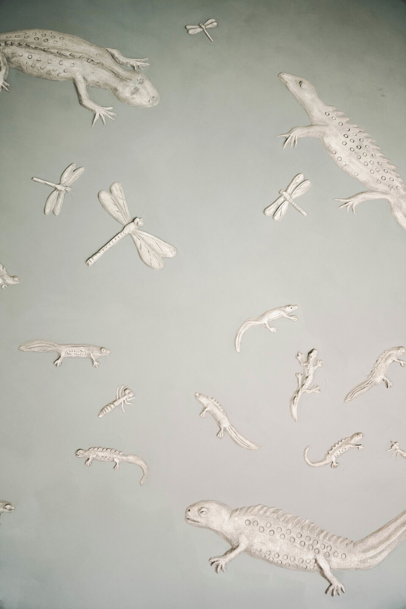 Een muur met diverse sculpturen van witte reptielen en insecten.