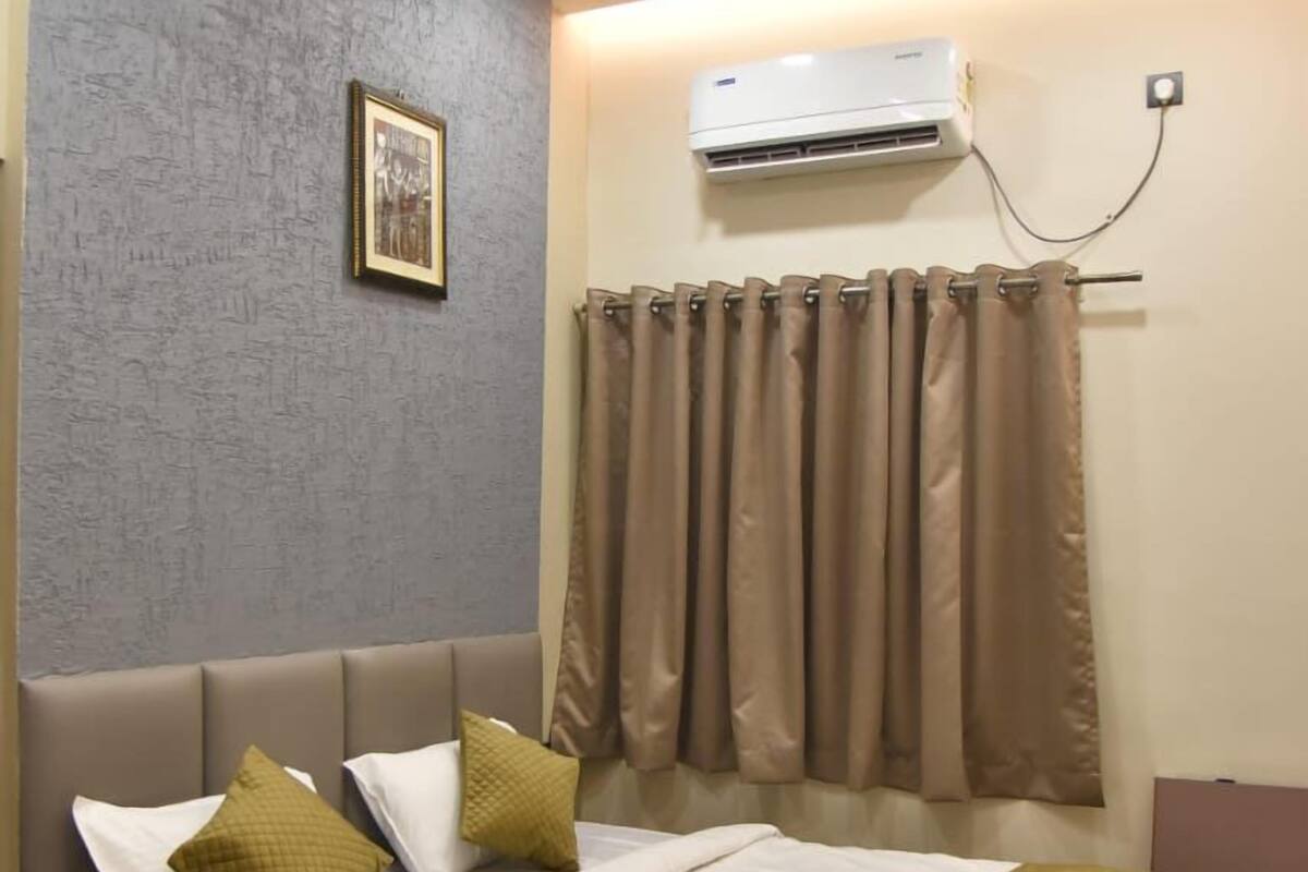 A neatly made bed with a white and green bedspread, a headboard, and two pillows. There is a ceiling fan above and an air conditioning unit on the wall.