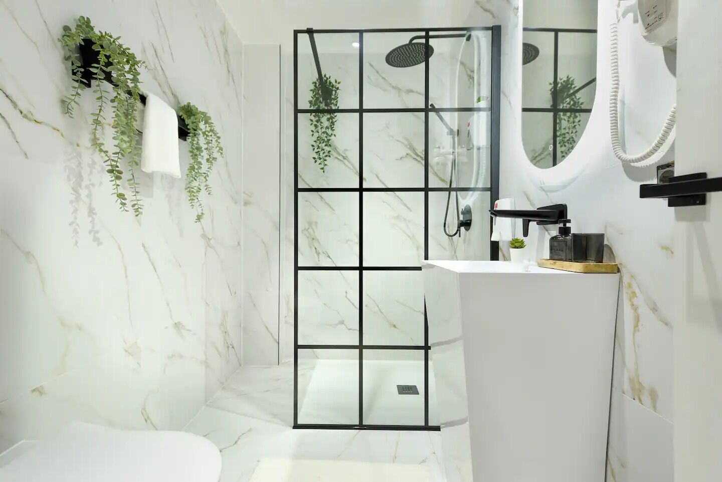 A modern bathroom with a glass shower enclosure, a white sink with a mirror, and green plants on the wall.