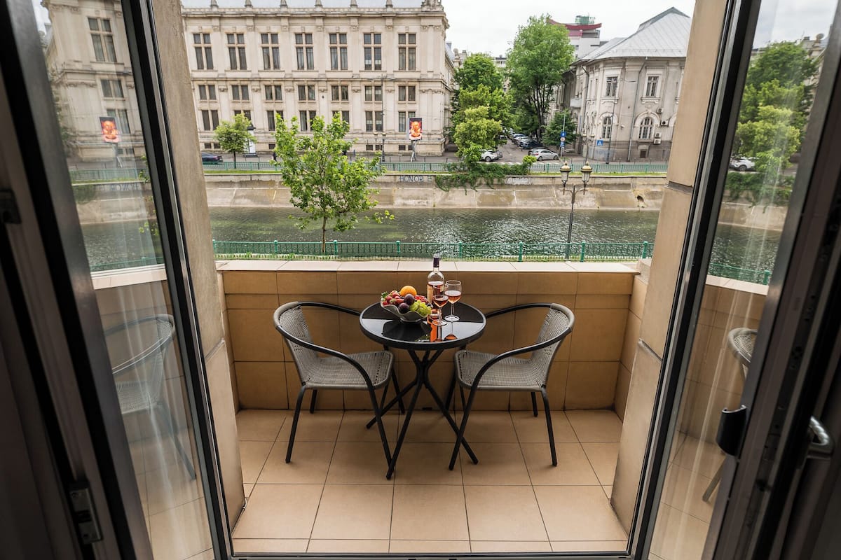 Un balcon avec une table dressée pour deux personnes, offrant une vue sur une rivière et des bâtiments historiques.